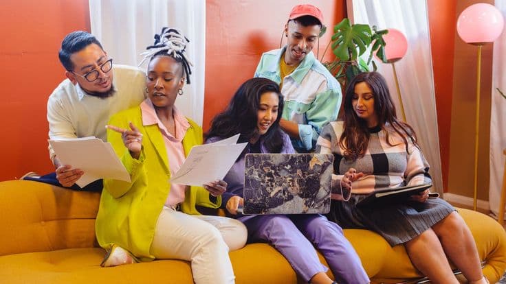 A small creative team talking through a brief together on a warm orange sofa