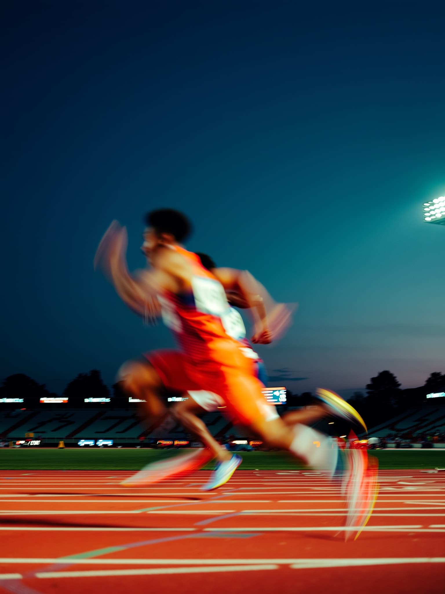 Sprinters streaking into long-exposure blur against a sharp dusk track